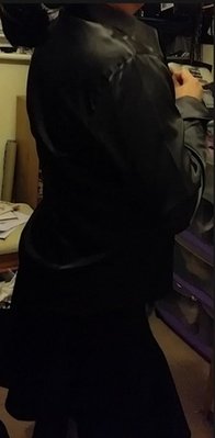 Shiny black satin blouse and pleated black skirt.... adjusting herself....